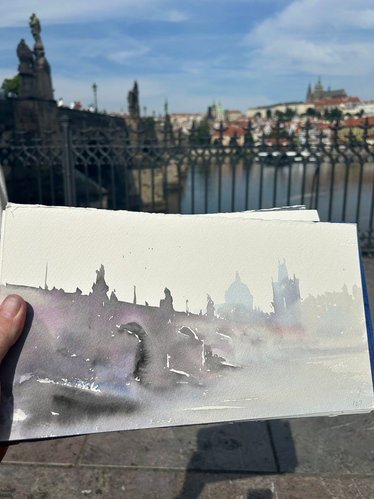 Acuarela de un puente de Praga sostenida frente al paisaje original