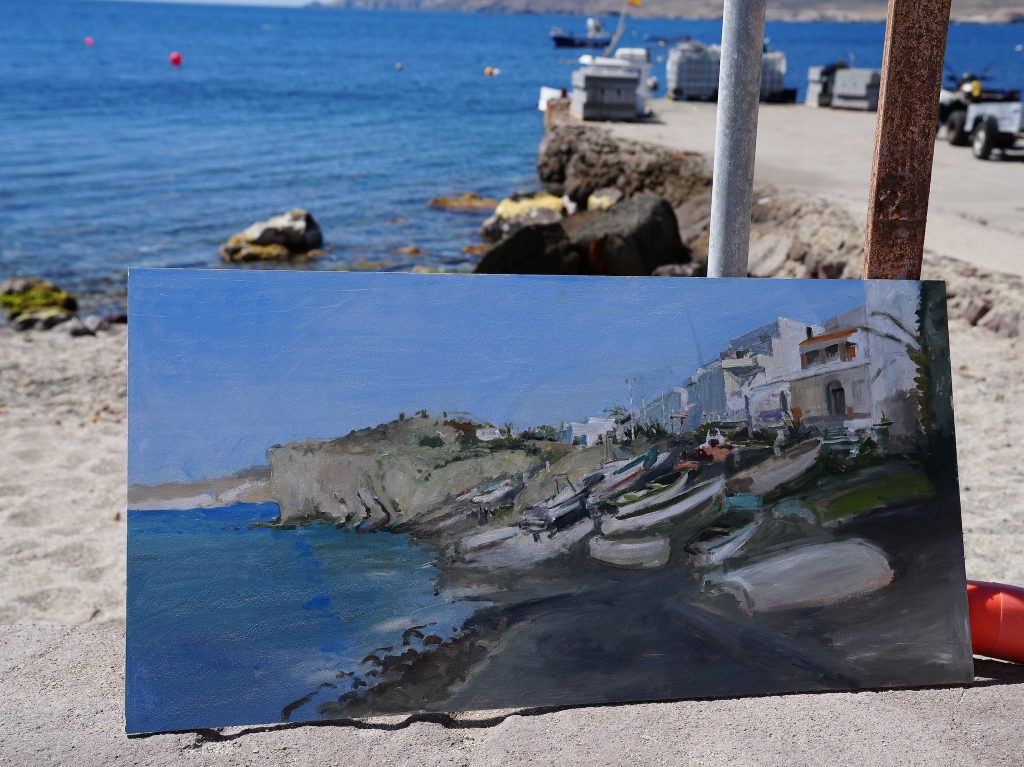 Pintura de barcas y casas costeras fotografiada junto al mar