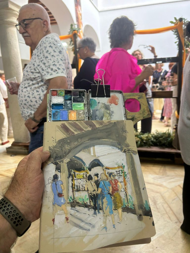 Cuaderno con una acuarela de personas reunidas bajo las arcadas de un patio
