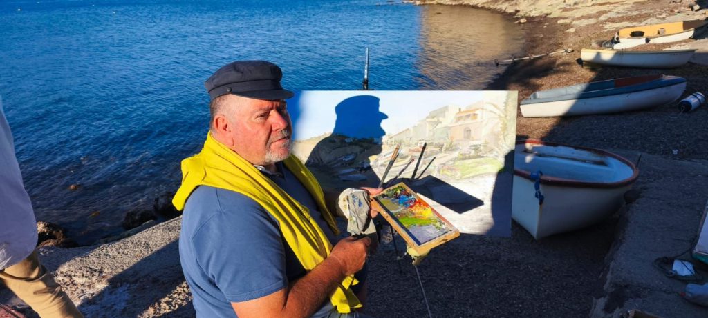 Pintor con paleta y caballete trabajando frente a las barcas de la costa