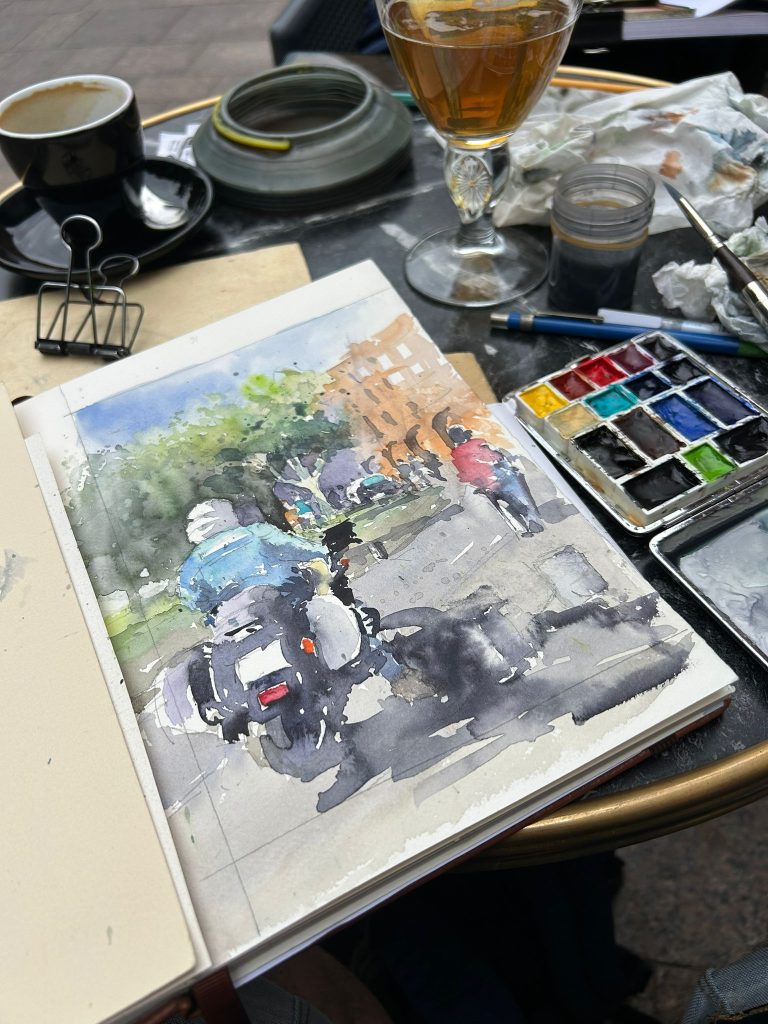 Detalle de una acuarela urbana con una moto y figuras junto a la paleta