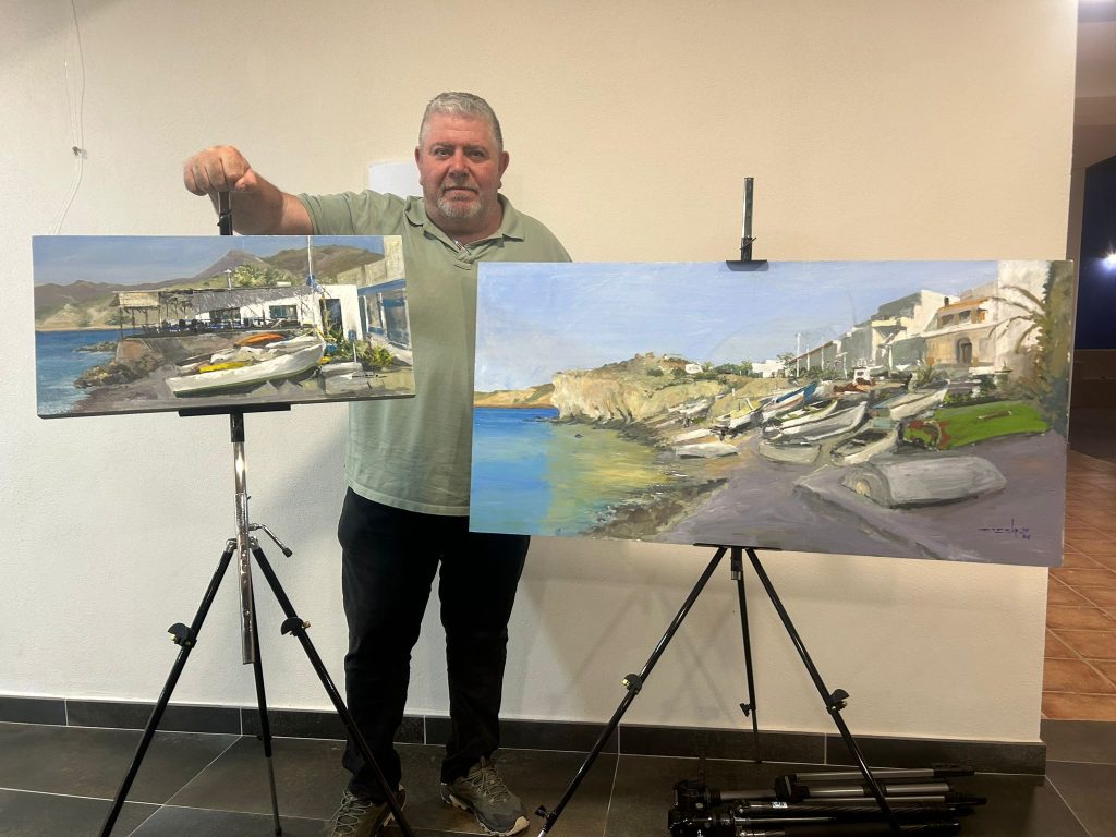 Juan Antonio López Morales mostrando dos pinturas de paisaje costero sobre caballetes